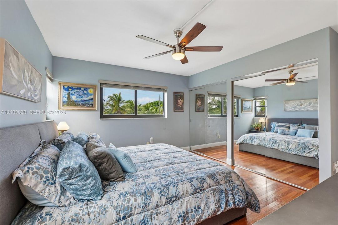Bedroom featuring wood-finish flooring, sliding mirrored closet doors, ceiling fan with integrated lighting, and horizontal windows