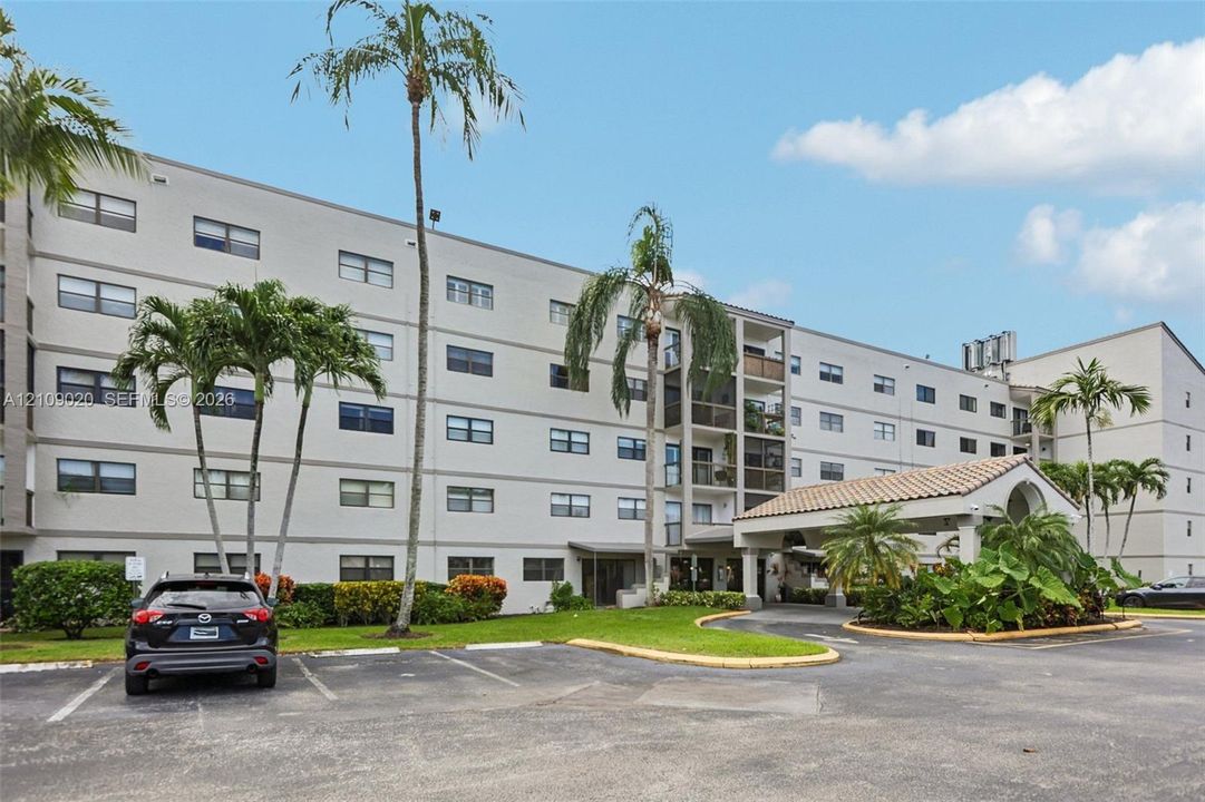 Multi-story residential building exterior featuring a covered porte-cochère, tiled roof detailing, and established palm trees