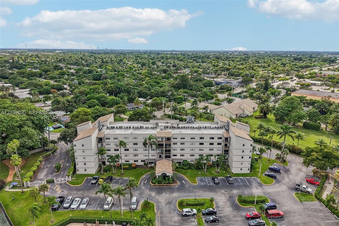 Multi-story residential building featuring a covered entryway, paved surface parking, and manicured landscaping with mature palm trees