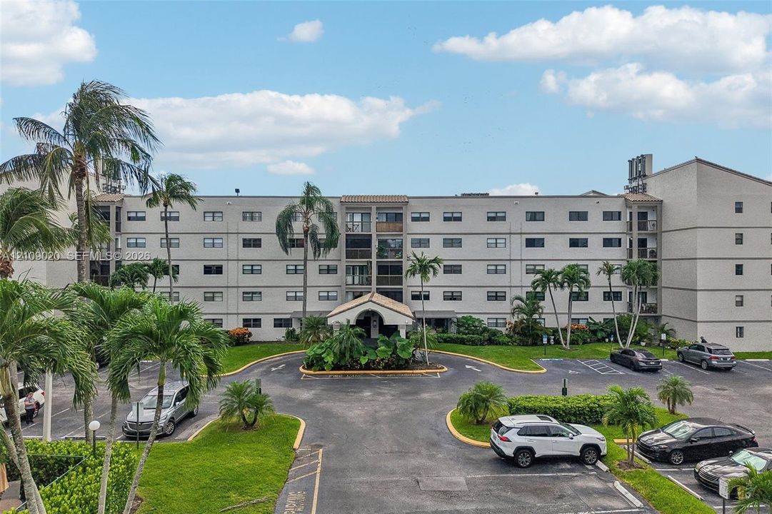 Multi-story residential building featuring a covered entryway, paved surface parking, and mature palm landscaping