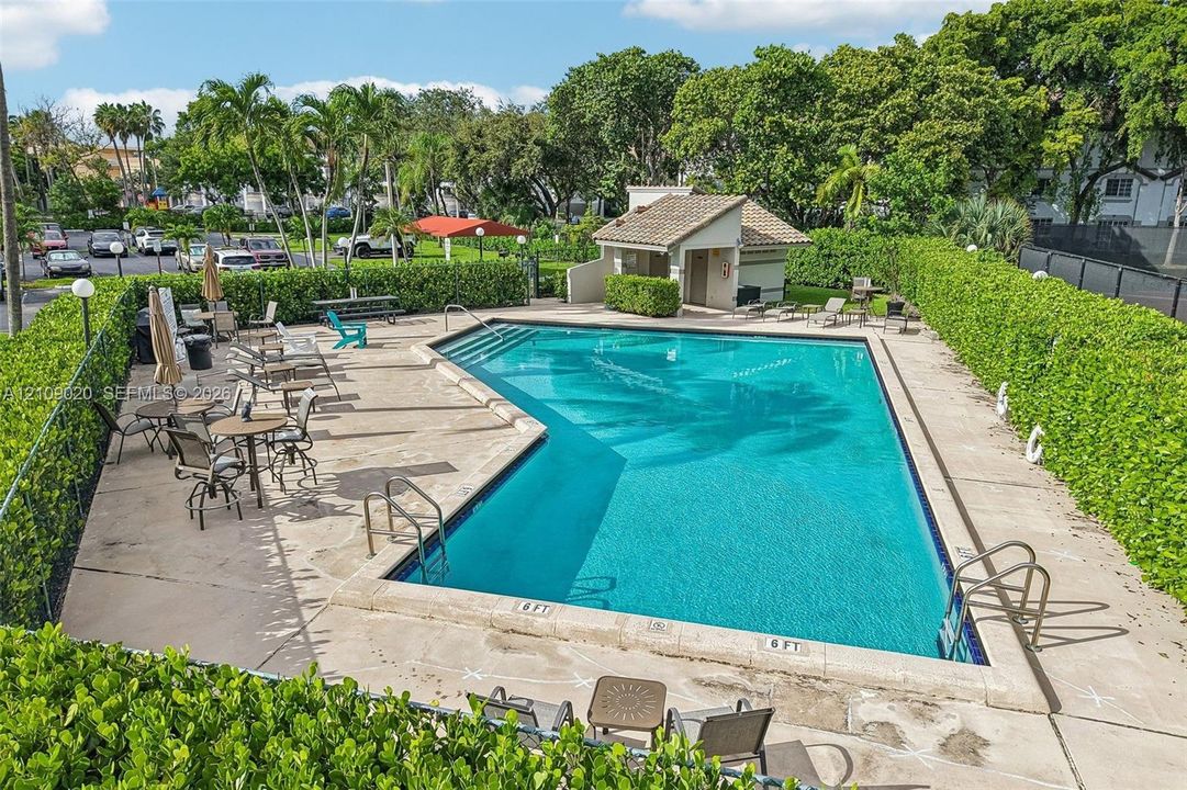 In-ground swimming pool with a concrete deck, enclosed by manicured privacy hedges and accompanied by a dedicated pool house