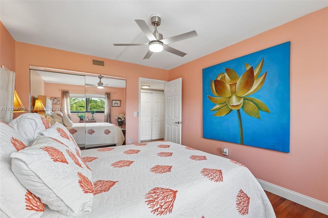 Bedroom featuring wood-finish flooring, a brushed nickel ceiling fan with integrated lighting, and mirrored closet doors