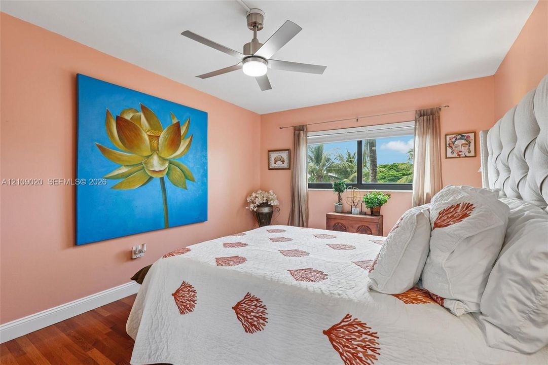 Wood-finish flooring, brushed metal ceiling fan with integrated lighting, and a horizontal window with exterior tropical greenery