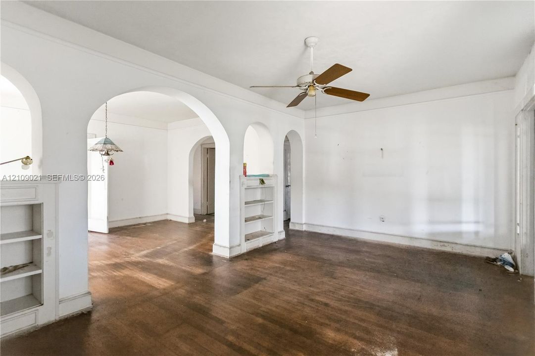 Interior featuring wood-finish flooring, multiple arched doorways, built-in shelving, and a ceiling-mounted fan
