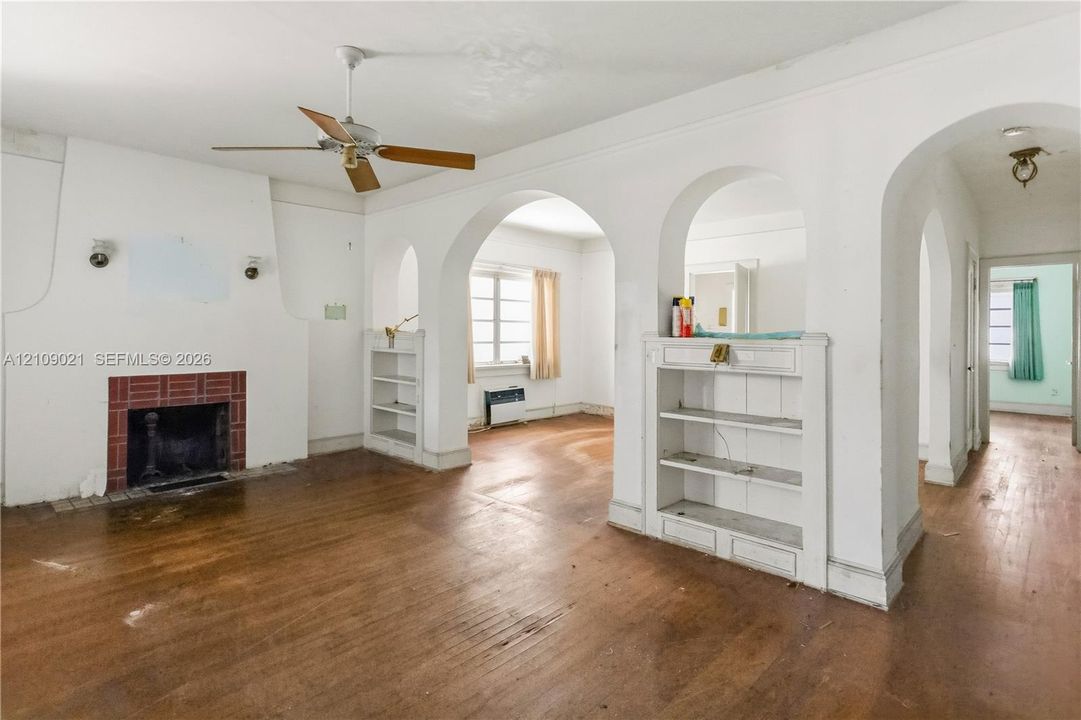 Architectural archways featuring built-in cabinetry, wood-finish flooring, and a fireplace with a brick surround