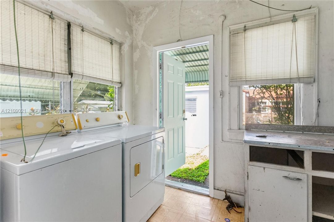 Laundry room featuring high-set windows with roller shades, a six-panel exterior door, and a built-in cabinetry unit with a flat-surface countertop