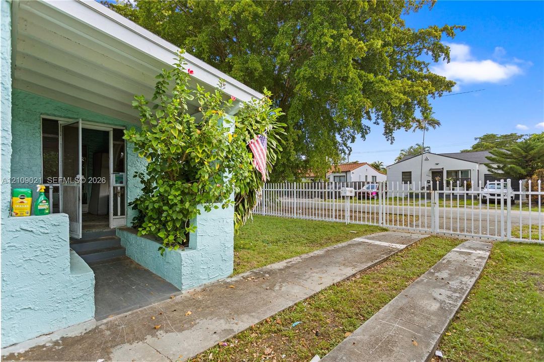 Exterior featuring a covered porch, textured stucco facade, concrete driveway, and white metal fencing