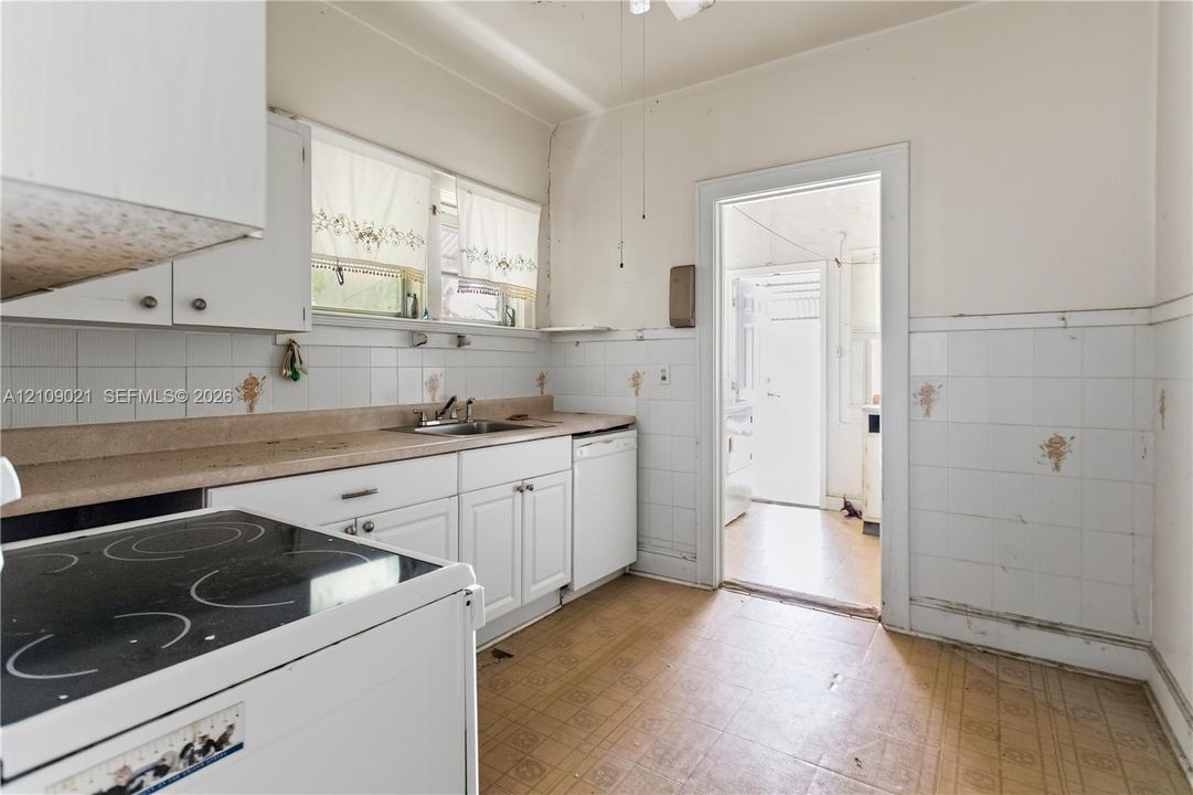 Kitchen featuring white shaker-style cabinetry, square tile wall backsplash, integrated metal sink, and white appliances
