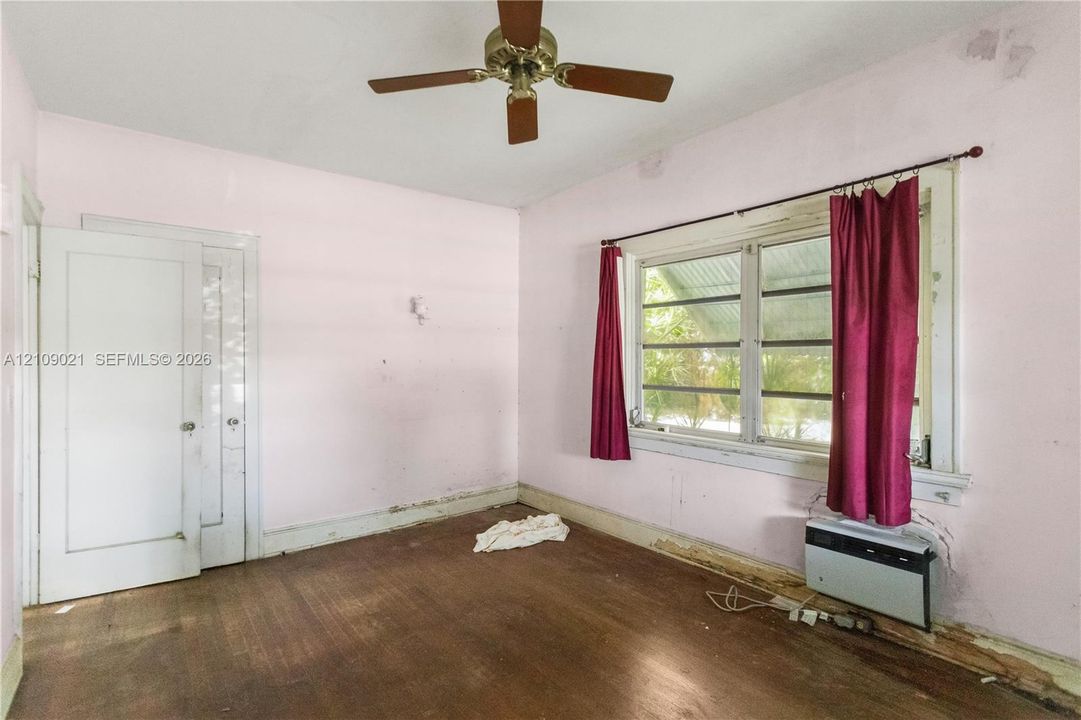 Room featuring wood-finish flooring, a multi-pane window with wood casing, a mounted wall-unit air conditioner, and a ceiling fan