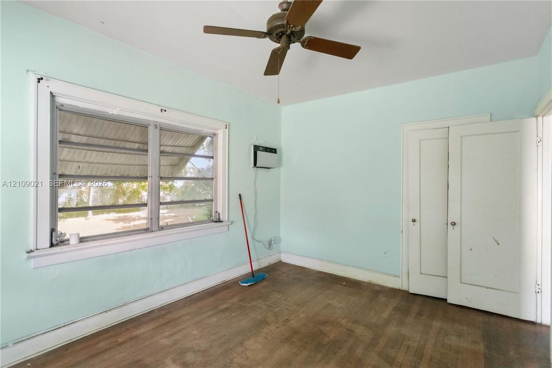 Wood-finish flooring, multi-pane window with exterior awning, ceiling fan with light fixture, and double-door closet