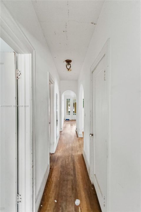 Hallway featuring wood-finish flooring, arched doorways, and flush-mount ceiling lighting