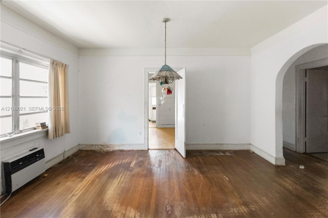 Room featuring wood-finish flooring, multi-pane window, arched doorway, and decorative pendant light fixture