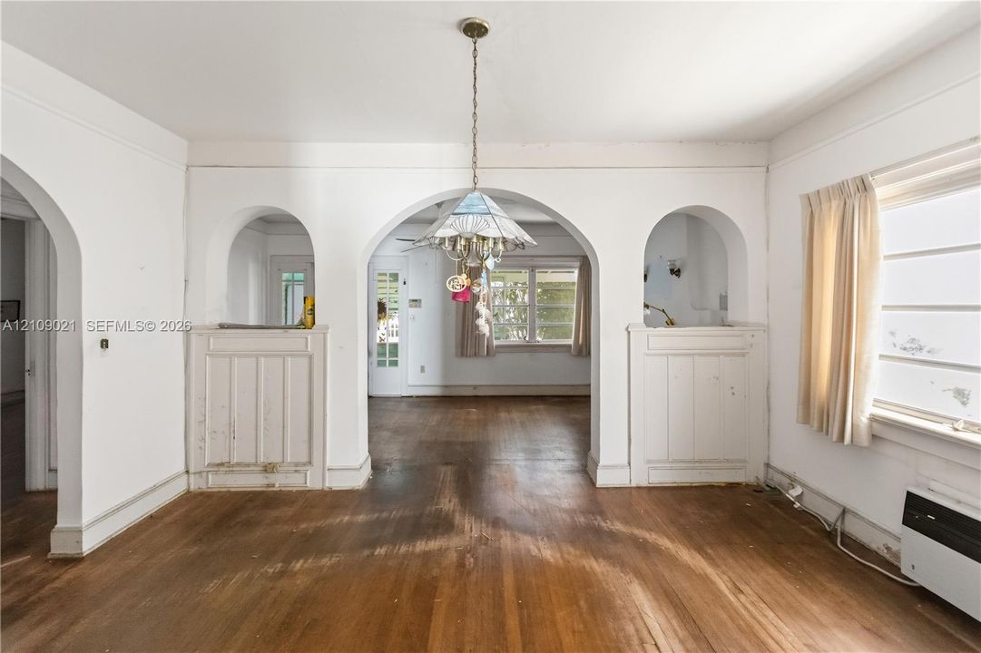 Interior featuring architectural arched openings, wood-finish flooring, wainscoting details, and a multi-pane glass chandelier