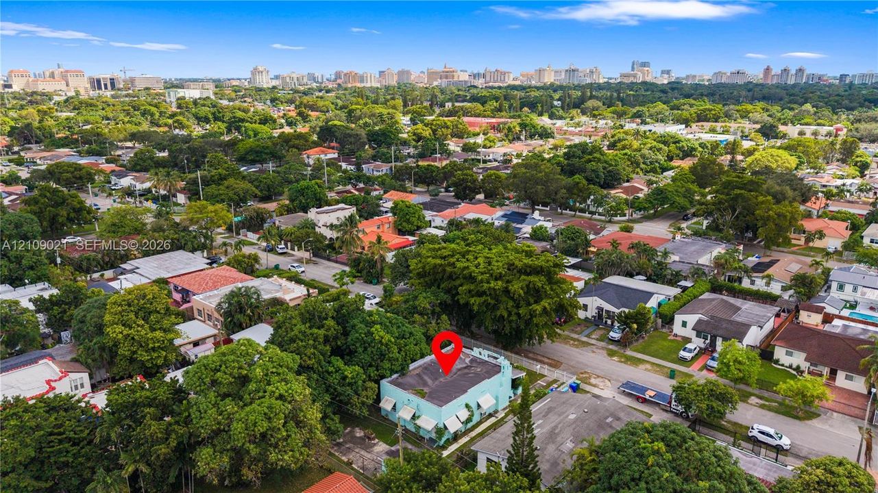 Aerial perspective of a corner lot property featuring a flat roof structure, exterior wall-mounted awnings, and mature landscaping