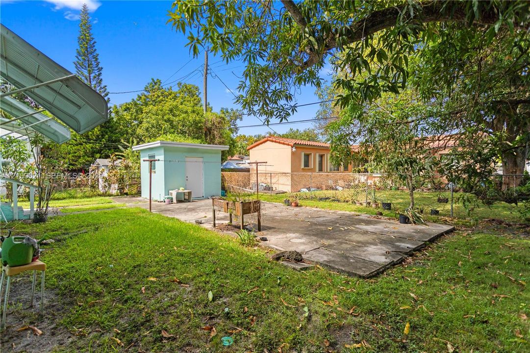 Backyard featuring a concrete patio, detached storage structure, mature trees, and perimeter fencing