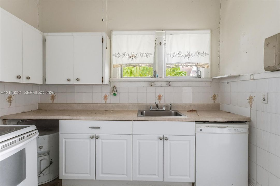 Kitchen featuring white cabinetry, neutral-toned countertops, tiled backsplash, stainless steel drop-in sink, and windows with double-pane glass