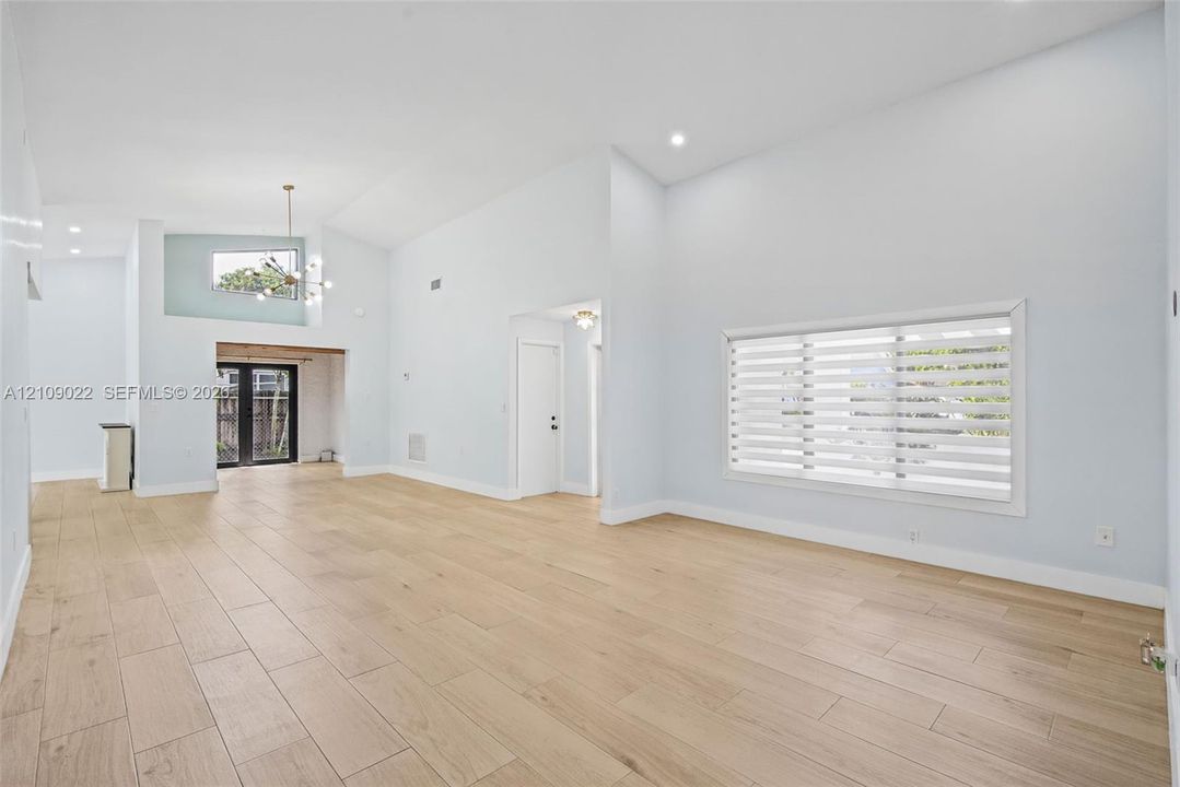 Vaulted ceilings, wood-finish flooring, recessed lighting, double French doors, and horizontal slat window treatments