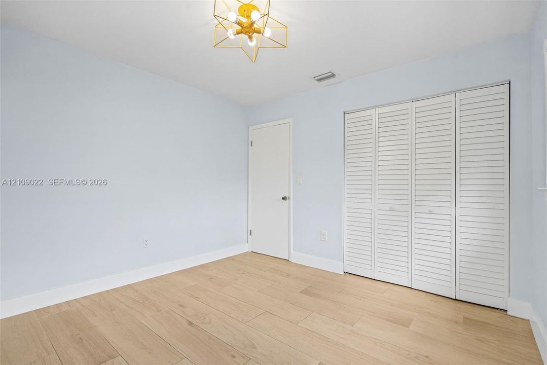 Neutral-toned room featuring wood-finish flooring, a geometric multi-bulb flush-mount light fixture, and a white interior door with a sliding louvered-panel closet