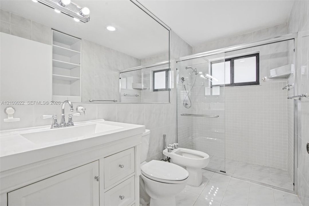 Bathroom featuring a white vanity with integrated basin, floor-to-ceiling mirror, recessed shelving, bidet, and a walk-in shower with a glass enclosure