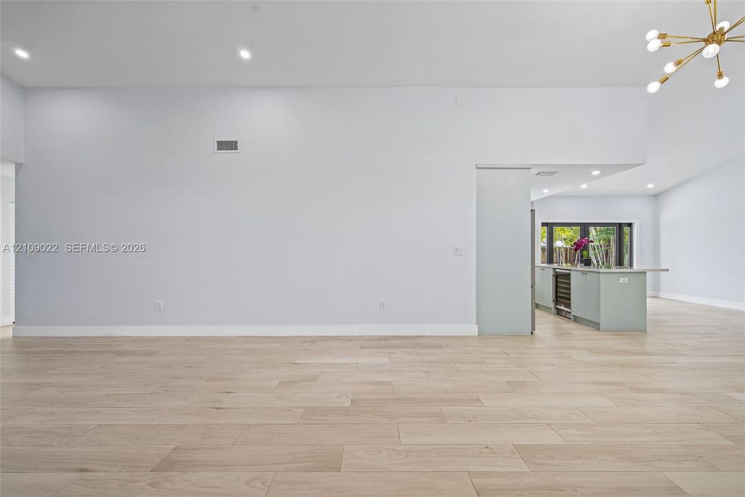 Open-concept interior featuring wood-finish flooring, recessed lighting, a modern multi-arm sputnik chandelier, and a kitchen island with a built-in wine cooler