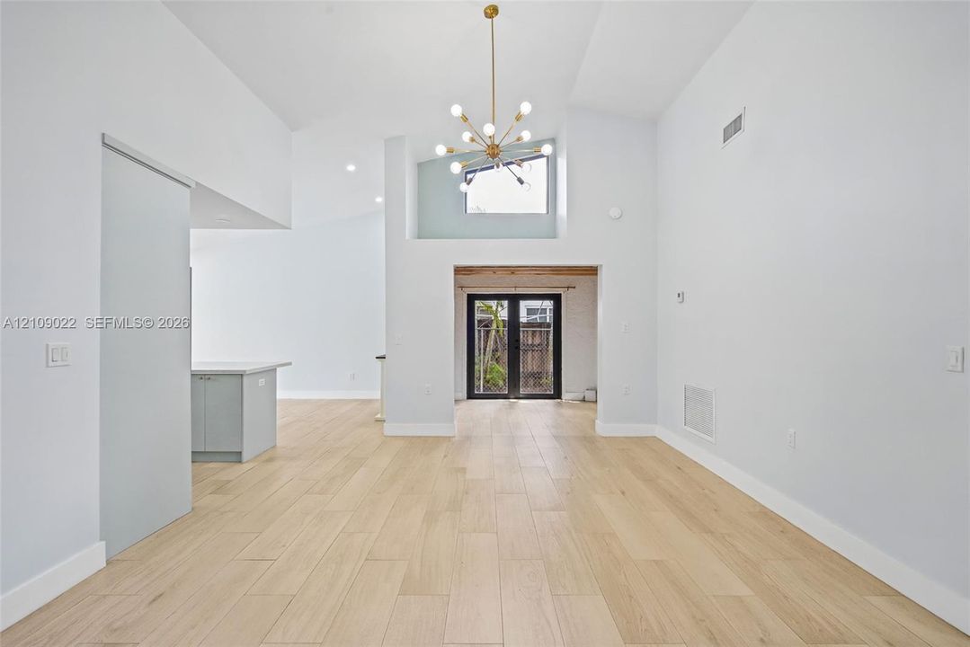 Vaulted ceilings, wood-finish flooring, multi-arm metallic chandelier, recessed lighting, and double glass-pane doors
