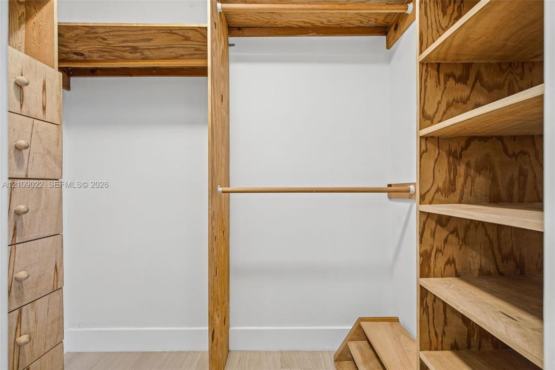 Custom wood-finish storage system featuring integrated shelving units, a built-in drawer stack, a hanging rod, and elevated shoe storage