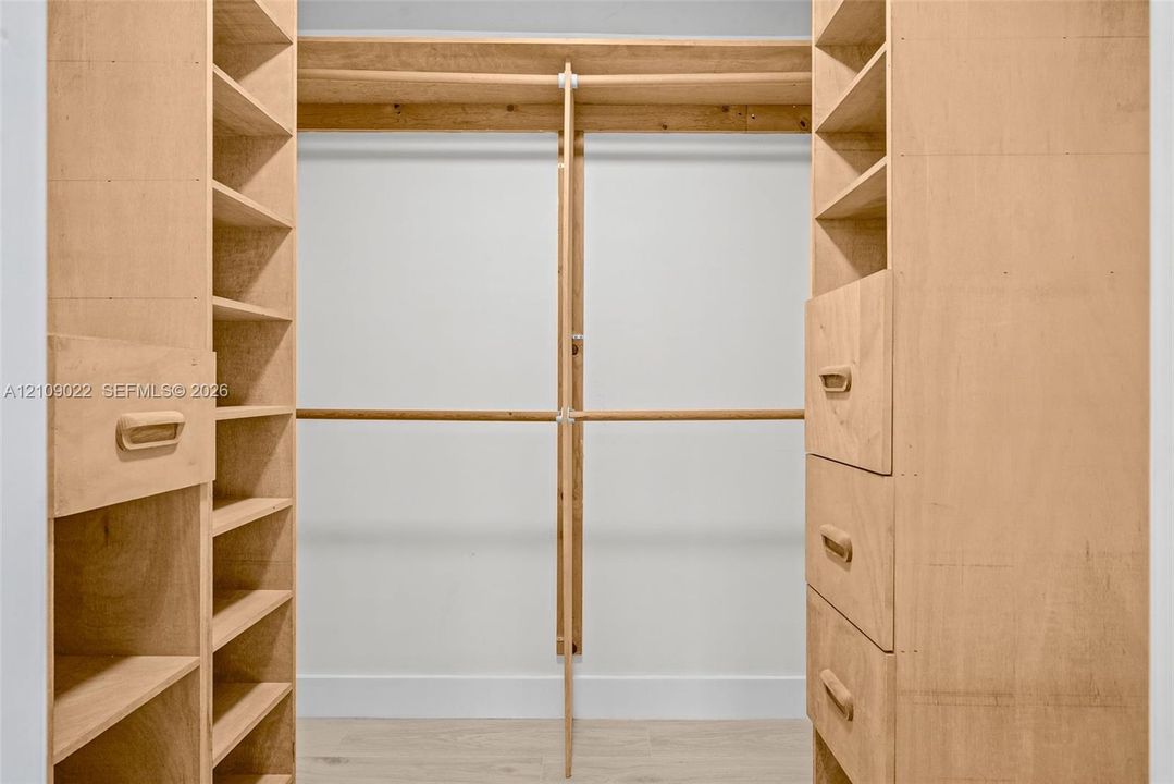 Custom closet featuring wood-finish cabinetry, floor-to-ceiling open shelving, integrated drawer storage, and dual-level hanging rods