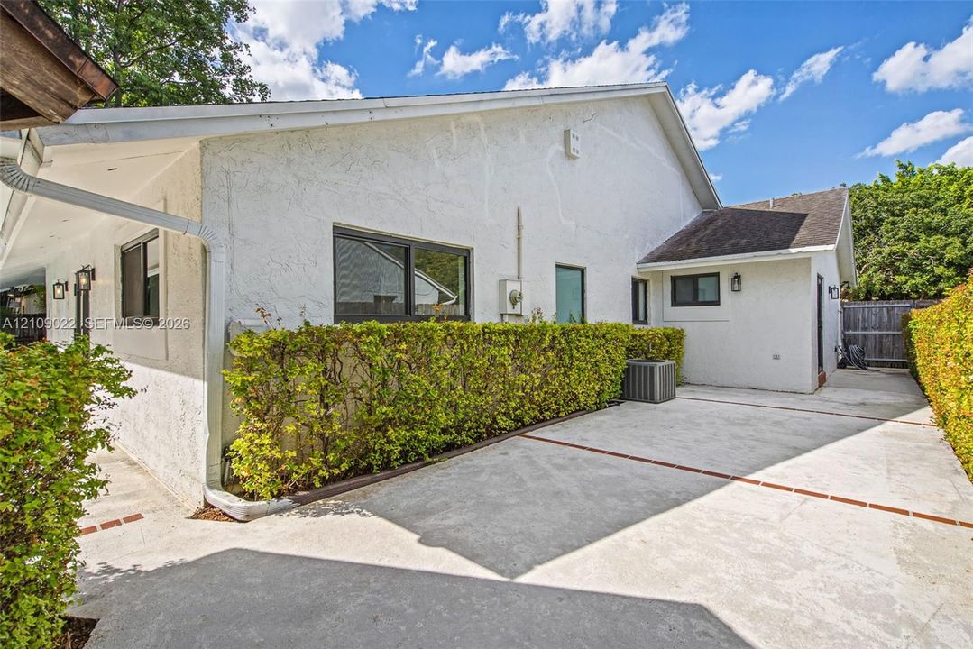 Stucco exterior featuring an expansive paved courtyard, brick-accented hardscaping, mature privacy hedges, and dark-framed windows
