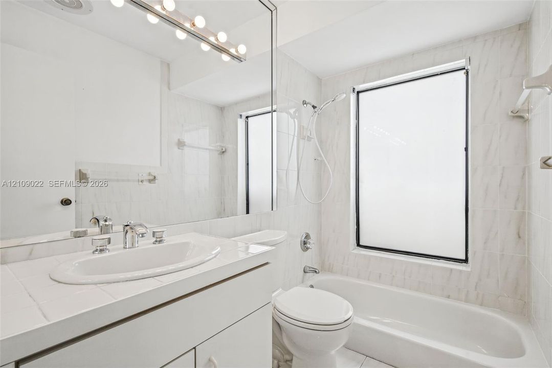 Bathroom featuring a wall-to-wall mirror, built-in vanity with an integrated basin, multi-bulb vanity light fixture, and a tiled shower-tub combination