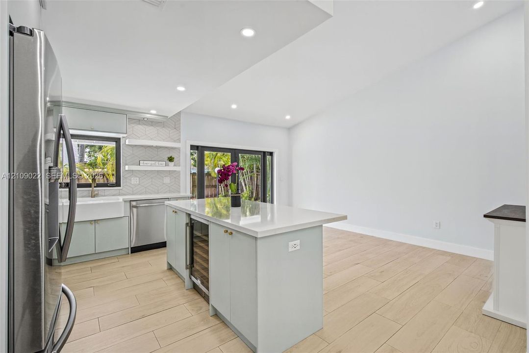 Kitchen featuring a center island with a stone countertop and built-in wine cooler, farmhouse-style sink, geometric tile backsplash with floating shelving, and wood-finish flooring
