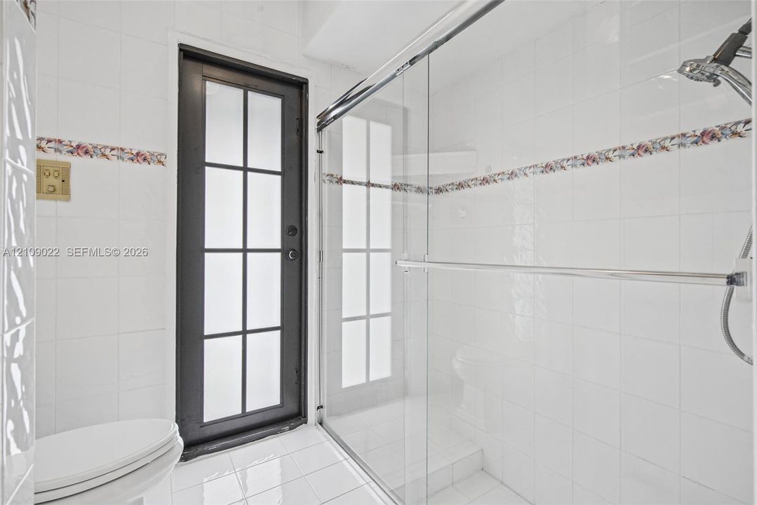 Bathroom featuring white wall tiling with floral inlay accents, a walk-in shower with a sliding glass door, a multi-pane glass-panel exterior door, and white tiled flooring