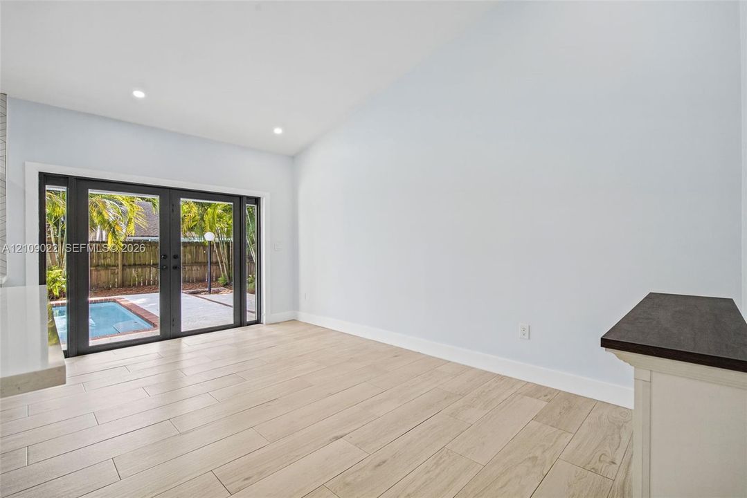Vaulted ceilings, wood-finish flooring, recessed lighting, and black-framed French doors opening to an exterior pool area