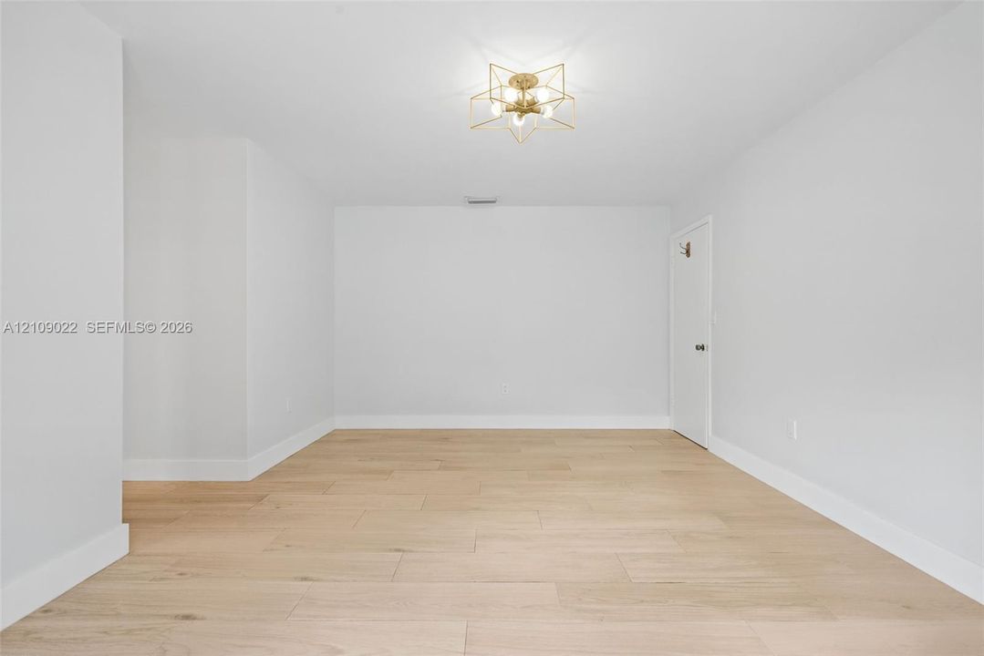 Neutral interior space featuring light-toned wood-finish flooring, a geometric gold-tone chandelier, and a crisp white finish