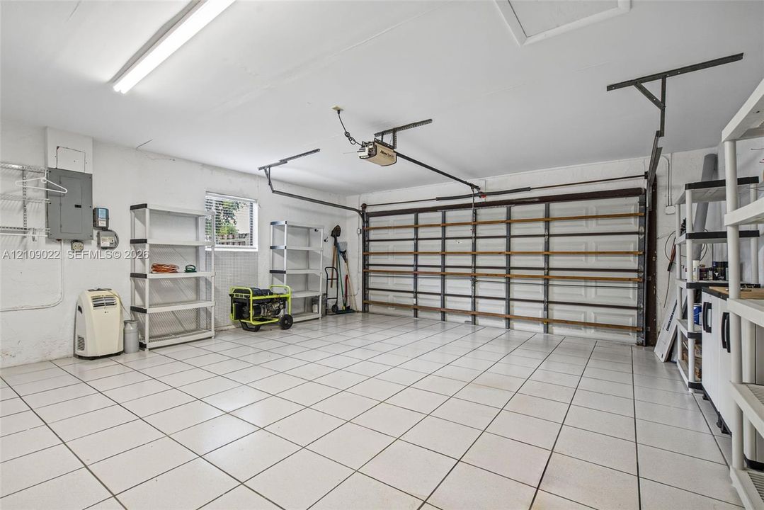 Attached garage featuring white tile flooring, a horizontal paneled door, integrated lighting, and electrical panel