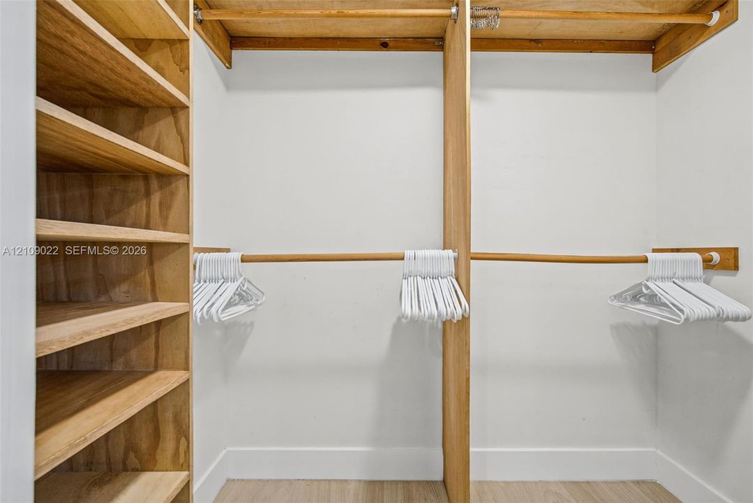 Walk-in closet featuring custom wood shelving units, integrated wooden garment rods, and light-toned wood-finish flooring