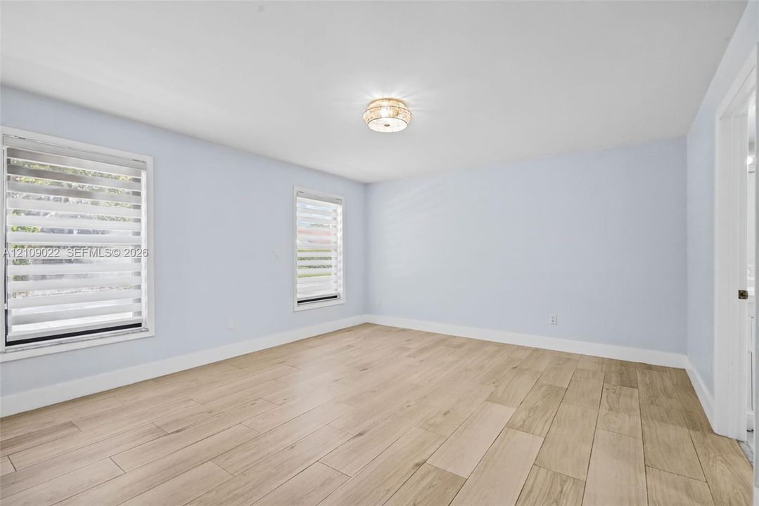 Neutral-toned room featuring wood-finish flooring, two windows with installed adjustable blinds, and a circular flush-mount ceiling light fixture
