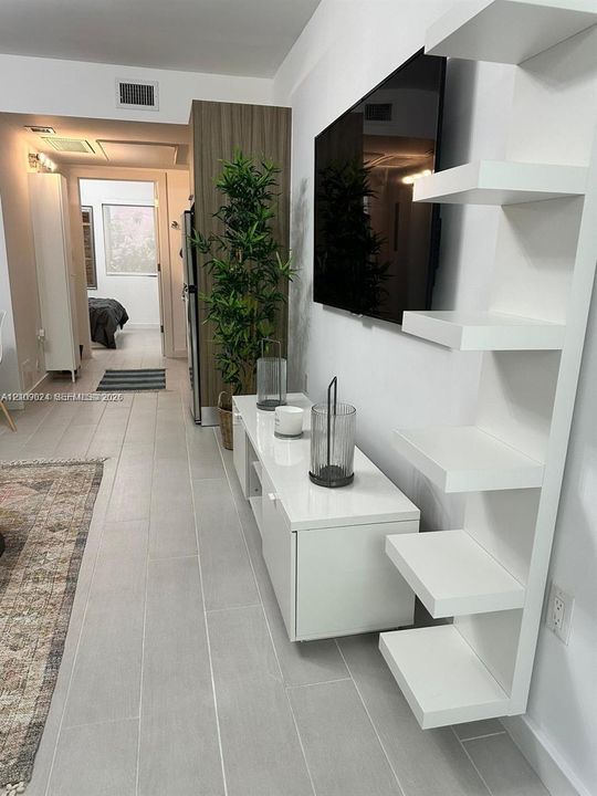 Custom white built-in shelving, high-gloss white media console, and neutral large-format tile flooring