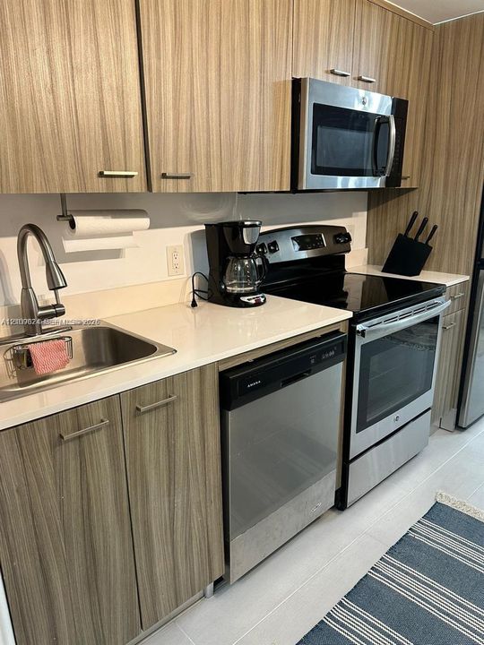 Kitchen featuring wood-finish cabinetry, stainless steel appliances, a solid-surface countertop, and a high-arc faucet with an integrated stainless steel undermount sink