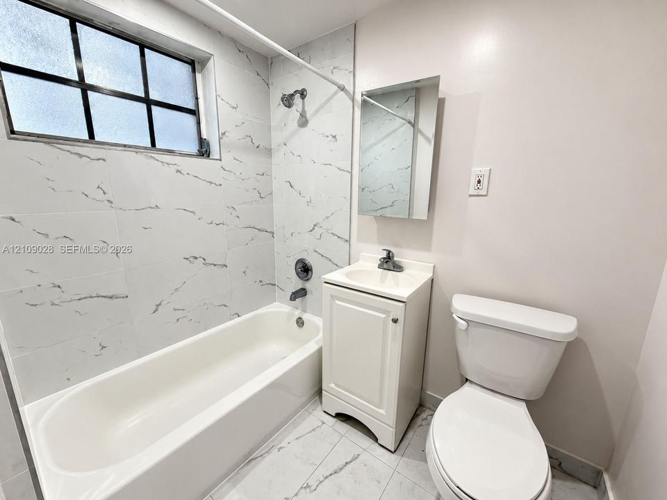Bathroom featuring a tub with stone-patterned tile surround, grid-pane window, pedestal vanity with sink, and floor-to-ceiling stone-patterned tile flooring
