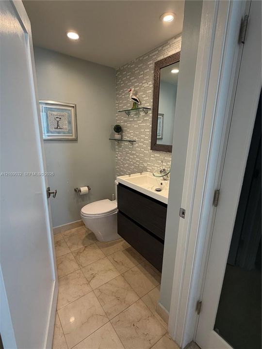 Floating vanity with dual soft-close drawers, stone-finish floor tiling, textured wall tile backsplash, integrated glass shelving, and recessed lighting