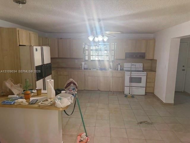 Kitchen featuring light-finish wood cabinetry, a peninsula, tile flooring, and integrated white appliances including a range and double-door refrigerator