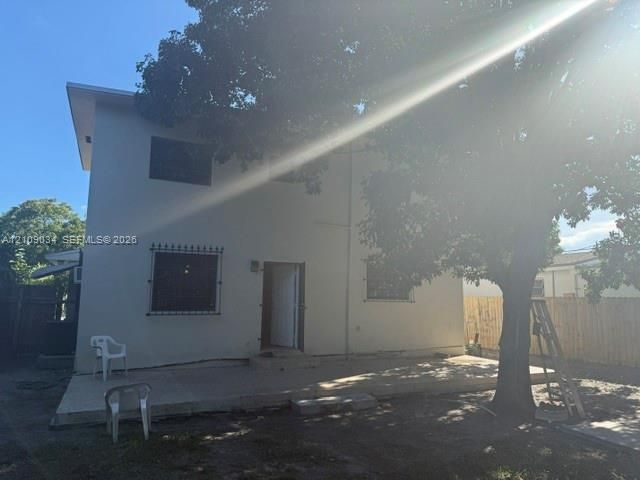 Stucco exterior, concrete patio, metal window security bars, and mature shade trees