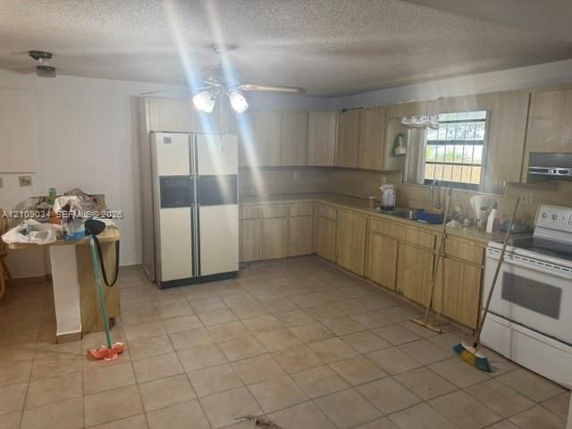 Kitchen featuring light-finish cabinetry, neutral tile flooring, built-in breakfast bar, and stainless steel sink