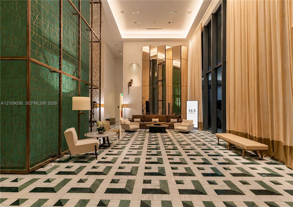 Grand lobby featuring double-height ceilings, intricate green geometric wall cladding, full-height window treatments, and patterned stone flooring