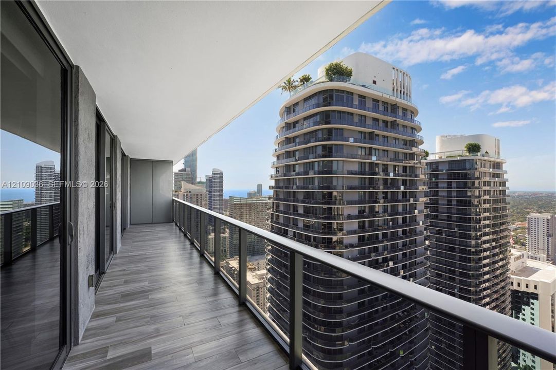 Covered balcony featuring wood-finish flooring, metal railing with glass panels, and floor-to-ceiling glass sliding doors