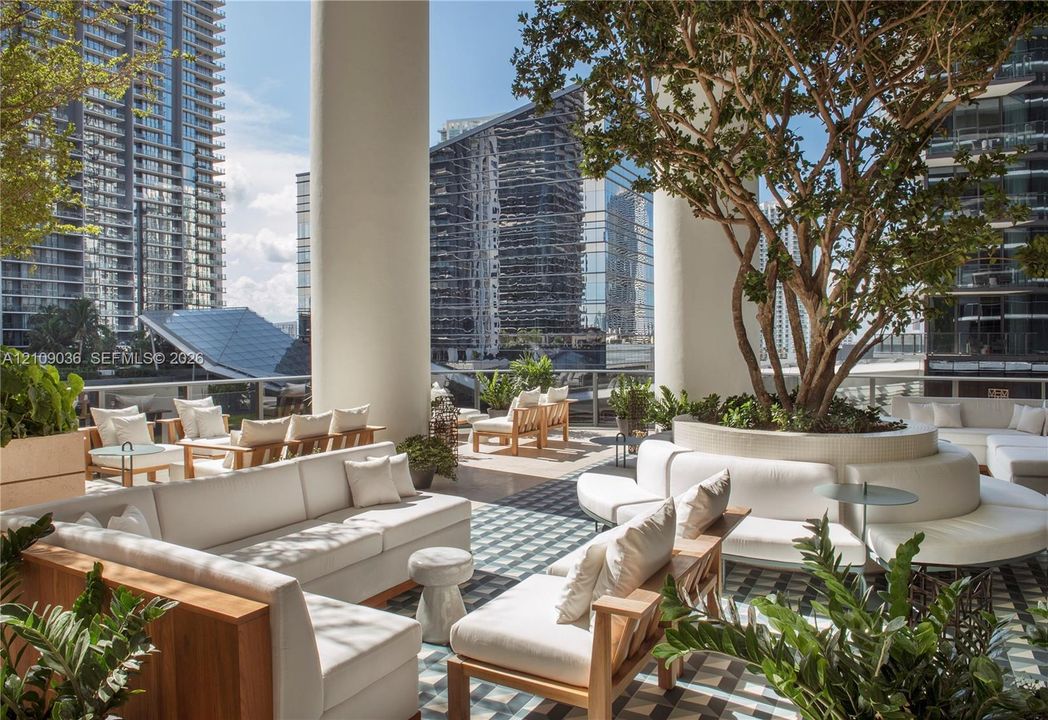 Expansive outdoor terrace featuring patterned tile flooring, structural concrete columns, and a circular raised planter containing a mature tree