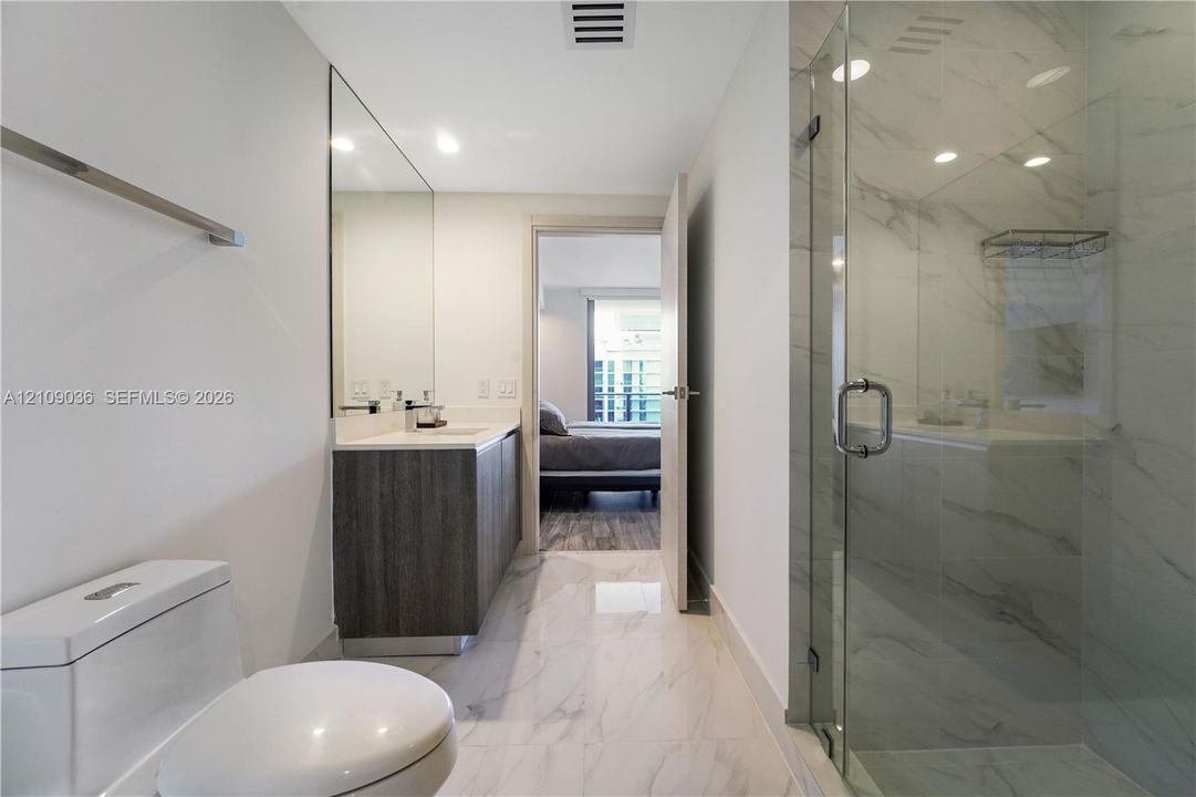 Bathroom featuring a dark wood-finish vanity, light-toned stone-style tile flooring, floor-to-ceiling vanity mirror, and a glass-enclosed shower with full-height stone-style wall tile