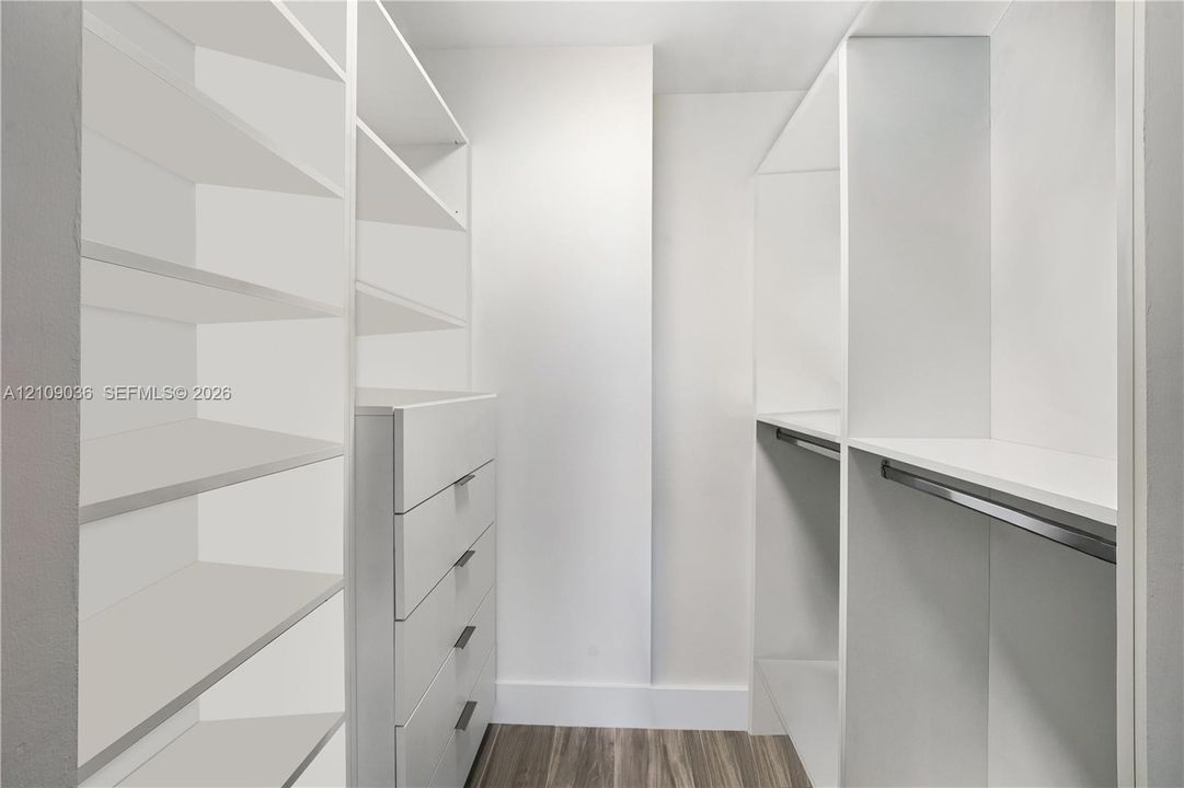 Walk-in closet featuring white built-in shelving, integrated dresser drawers with bar pulls, and a metal hanging rod over wood-finish flooring