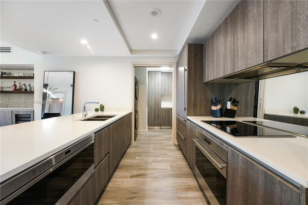 Modern kitchen featuring wood-finish cabinetry, white countertops, built-in stainless steel appliances, a mirrored backsplash, and wood-finish flooring