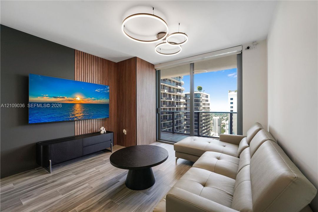 Living space featuring wood-finish flooring, floor-to-ceiling windows, modern multi-ring pendant lighting, and decorative wood-slat wall paneling